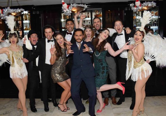 Group of people dressed up for their 1920s themed Christmas party in front of a hotel bar